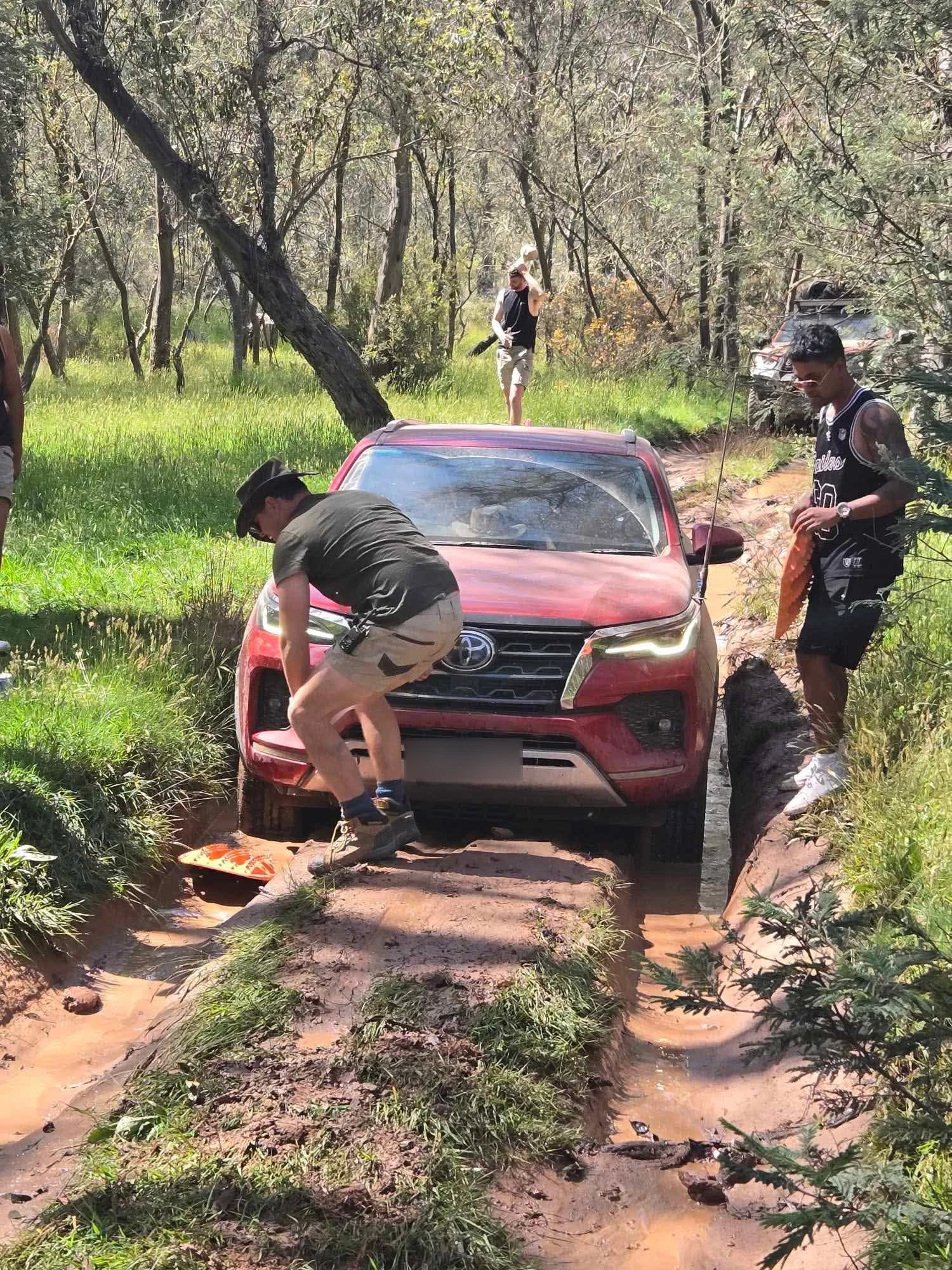 Red Toyota 4WD being guided through a muddy bush track on an off-road trip